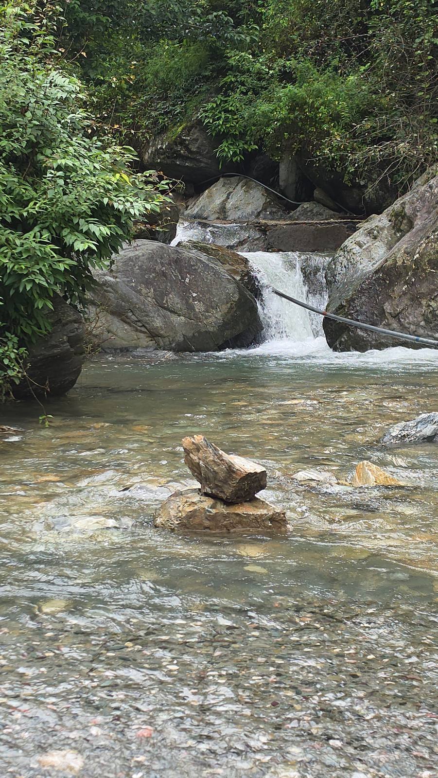 A small waterfall over boulders in the stream near Himtattva, with a stacked cairn in the foreground